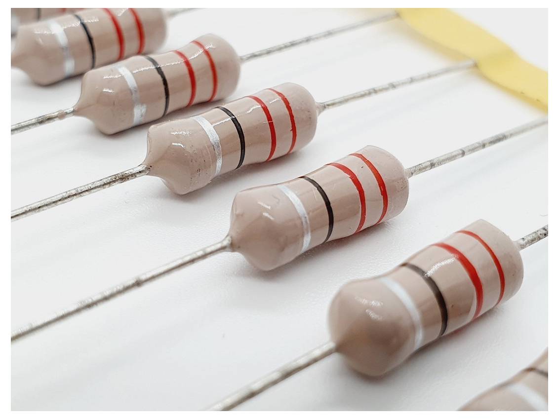 Nahaufnahme mehrerer elektronischer Widerstände, die nebeneinander aufgereiht sind, wobei jeder farbige Bänder zur Anzeige der Widerstandswerte auf einem weißen Hintergrund trägt.