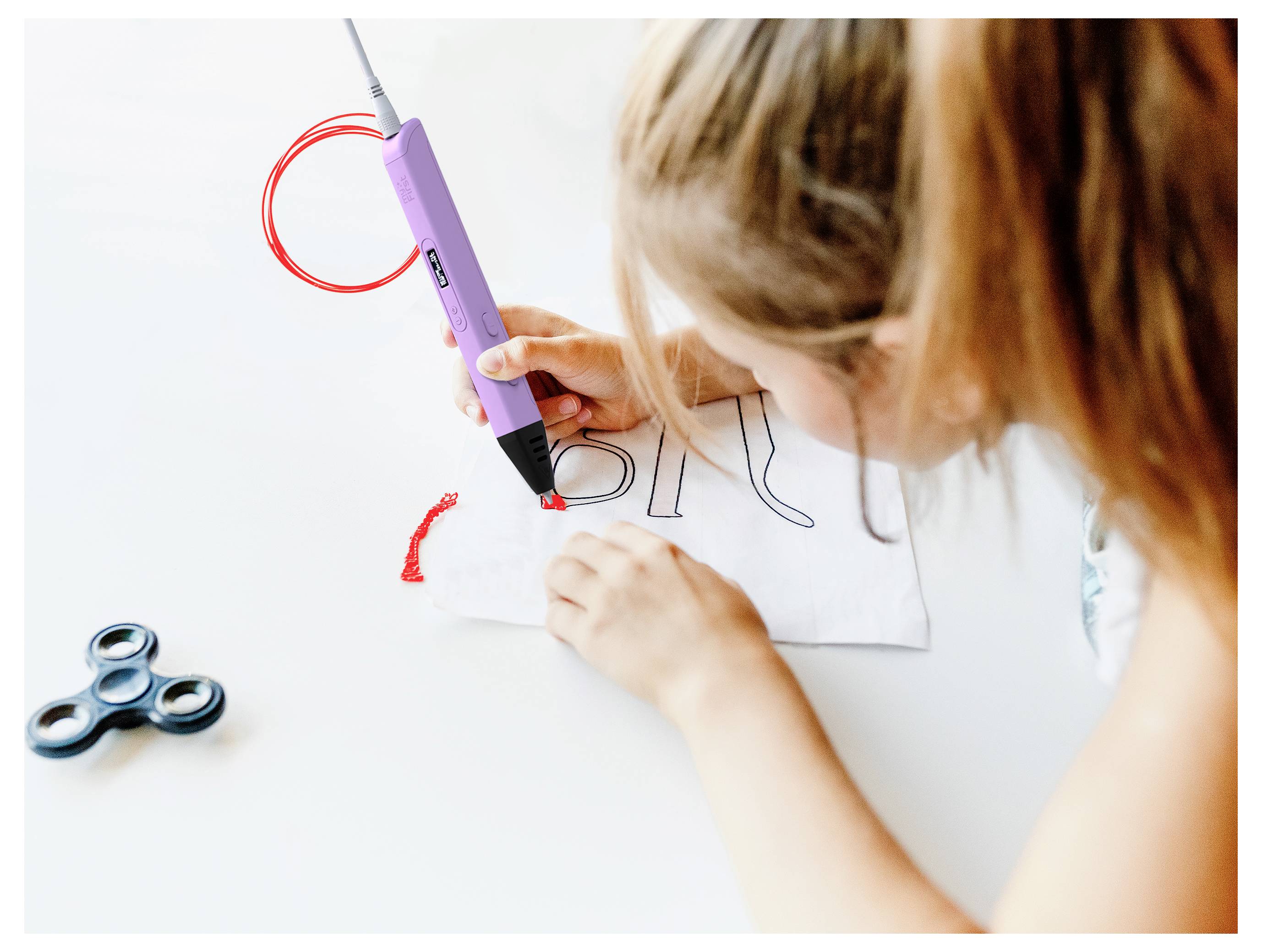 Ein Kind verwendet einen lila 3D-Stift, um eine Zeichnung auf Papier nachzuzeichnen. Ein Fidget Spinner liegt daneben auf dem Tisch.