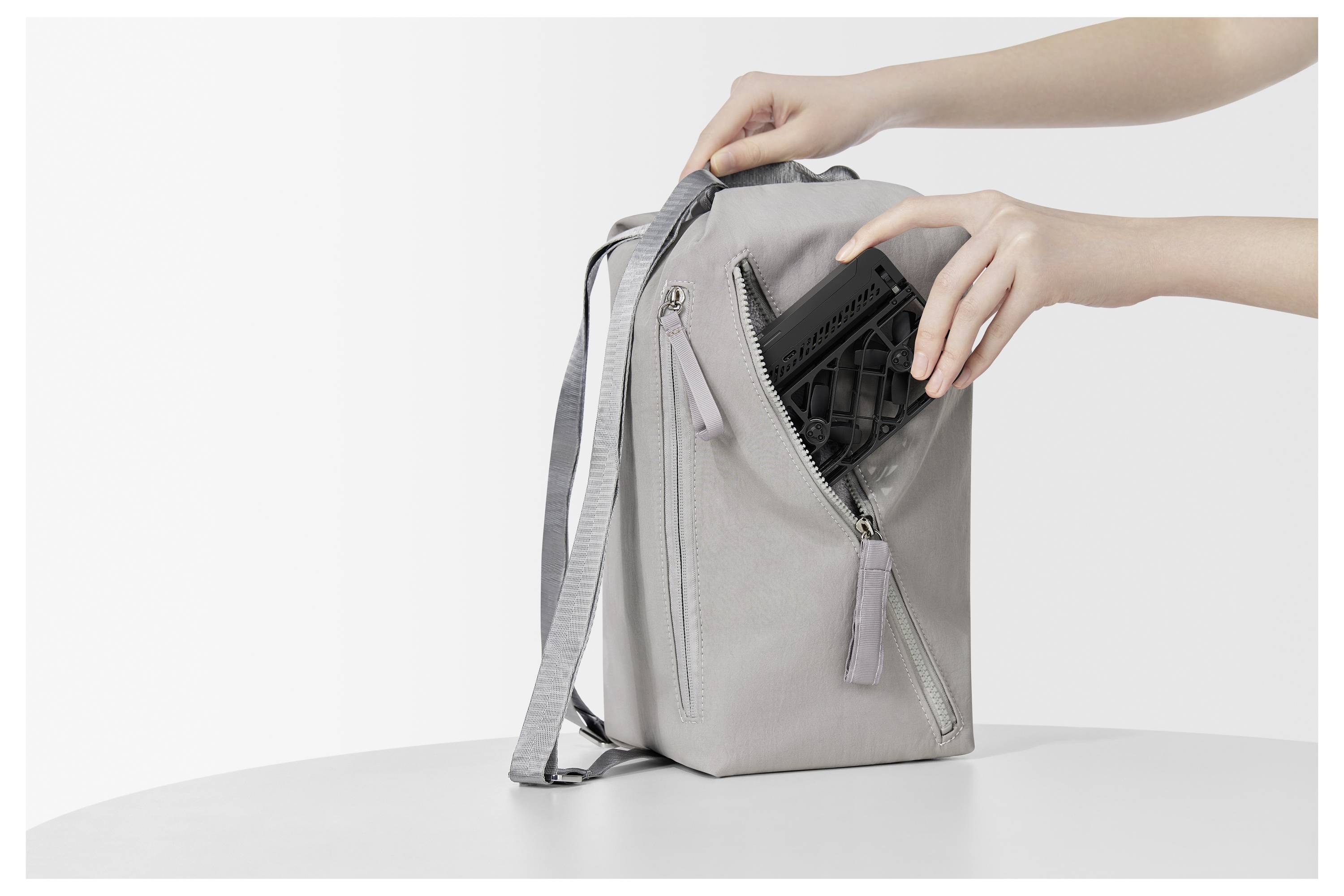 Eine Person legt ein Tablet in einen grauen Rucksack auf einem weißen Tisch und demonstriert damit die Staufunktion der Tasche.