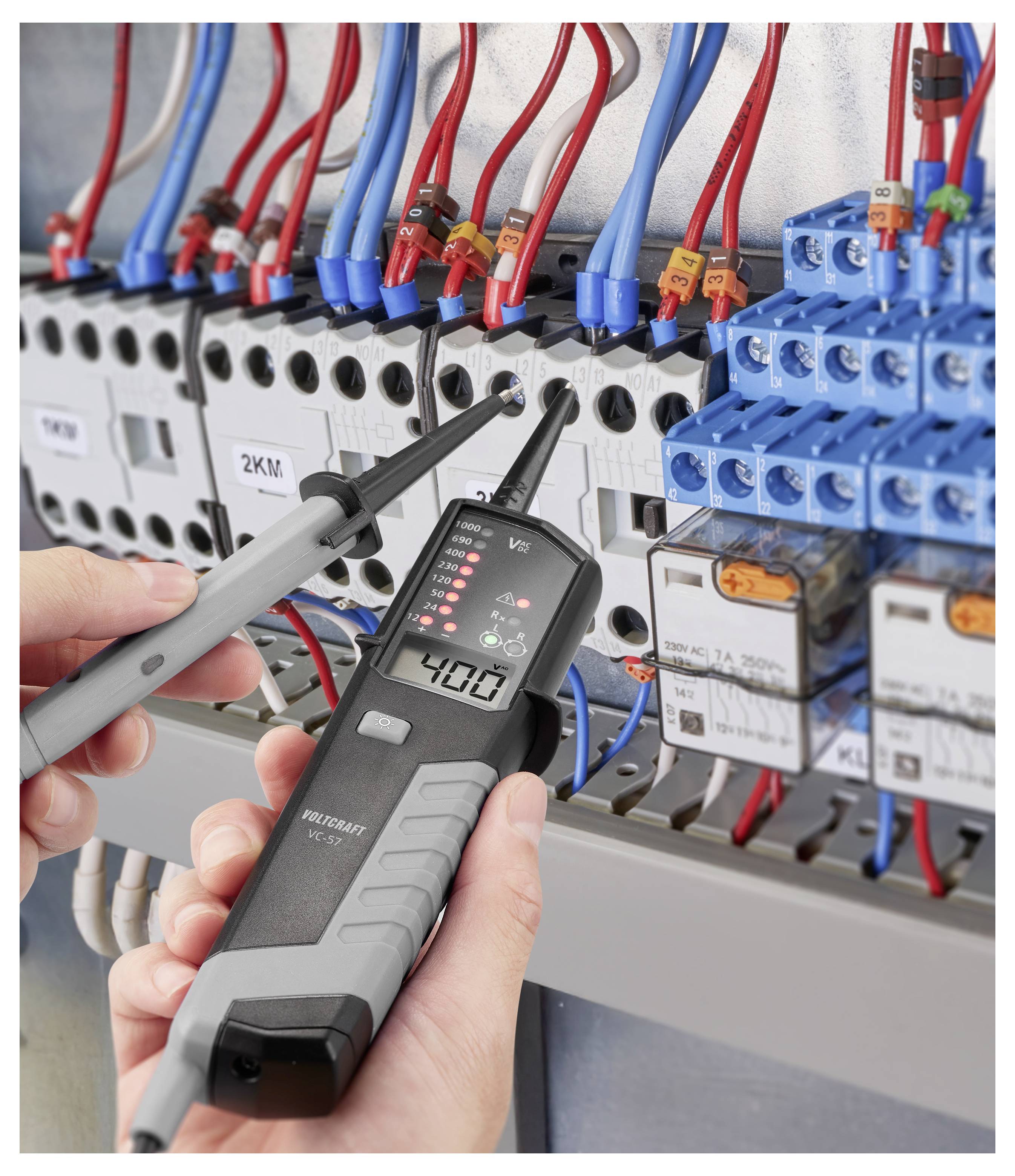 Techniker testet ein elektrisches Schaltschrank mit einer Spannungsprüfer-Sonde, umgeben von roten und blauen Drähten und Schaltkomponenten.
