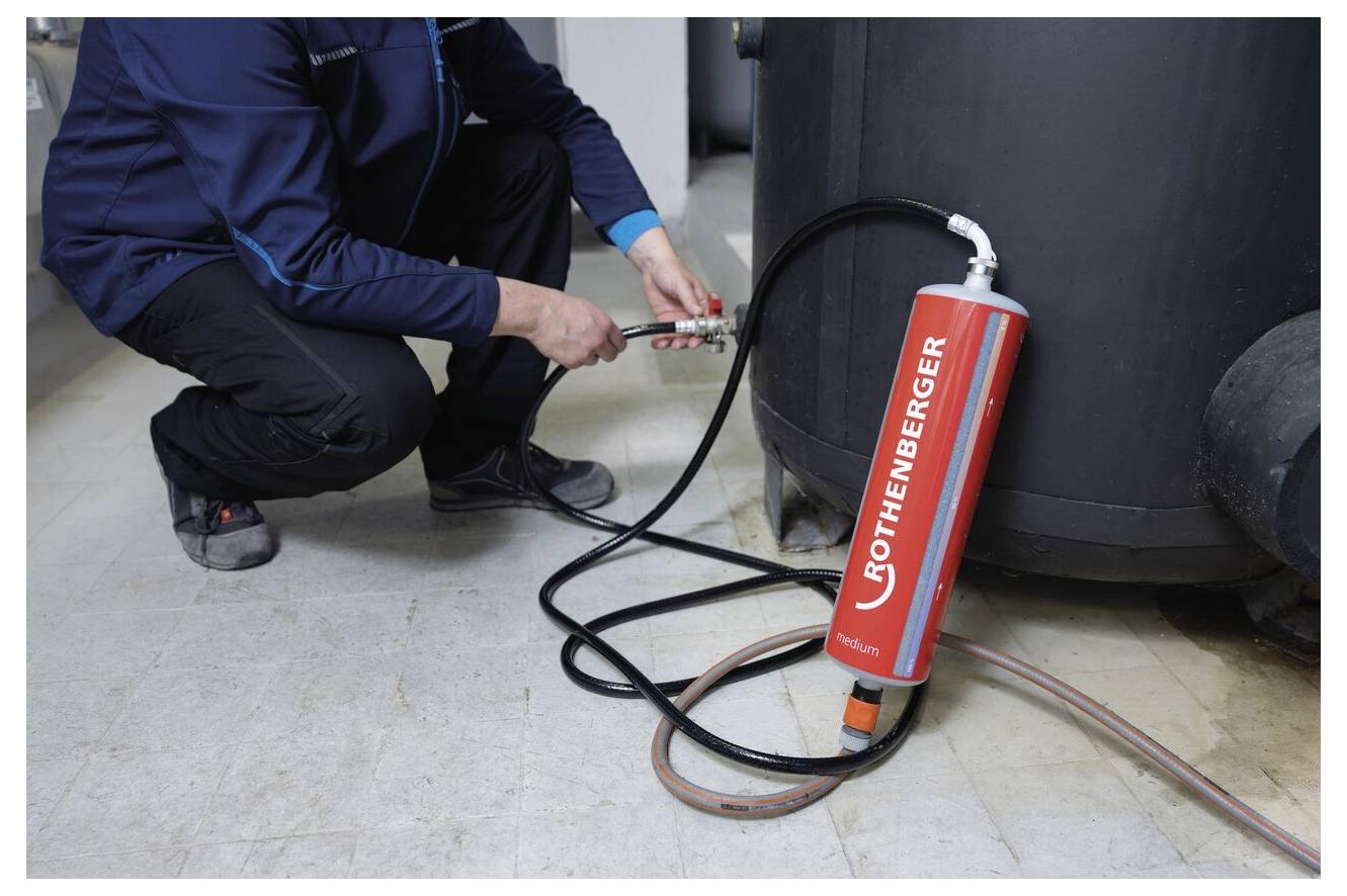 Eine Person schließt einen Schlauch an eine Rothenberger-Prüfpumpe in der Nähe eines großen zylindrischen Tanks an, um sich auf eine Druckprüfungsaufgabe vorzubereiten.