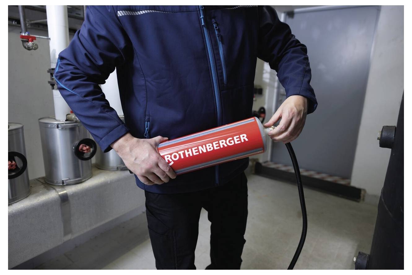 Eine Person, die ein großes rotes Werkzeug mit der Aufschrift "ROTHENBERGER" in einem Technikraum hält, möglicherweise im Begriff, Wartungsarbeiten durchzuführen.