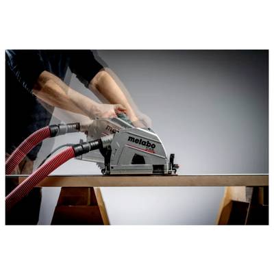 Eine Person, die ein Metabo-Elektrowerkzeug mit roten Absaugschläuchen verwendet, um entlang der Kante eines Holzbretts auf einer Werkbank zu schneiden oder zu schleifen.
