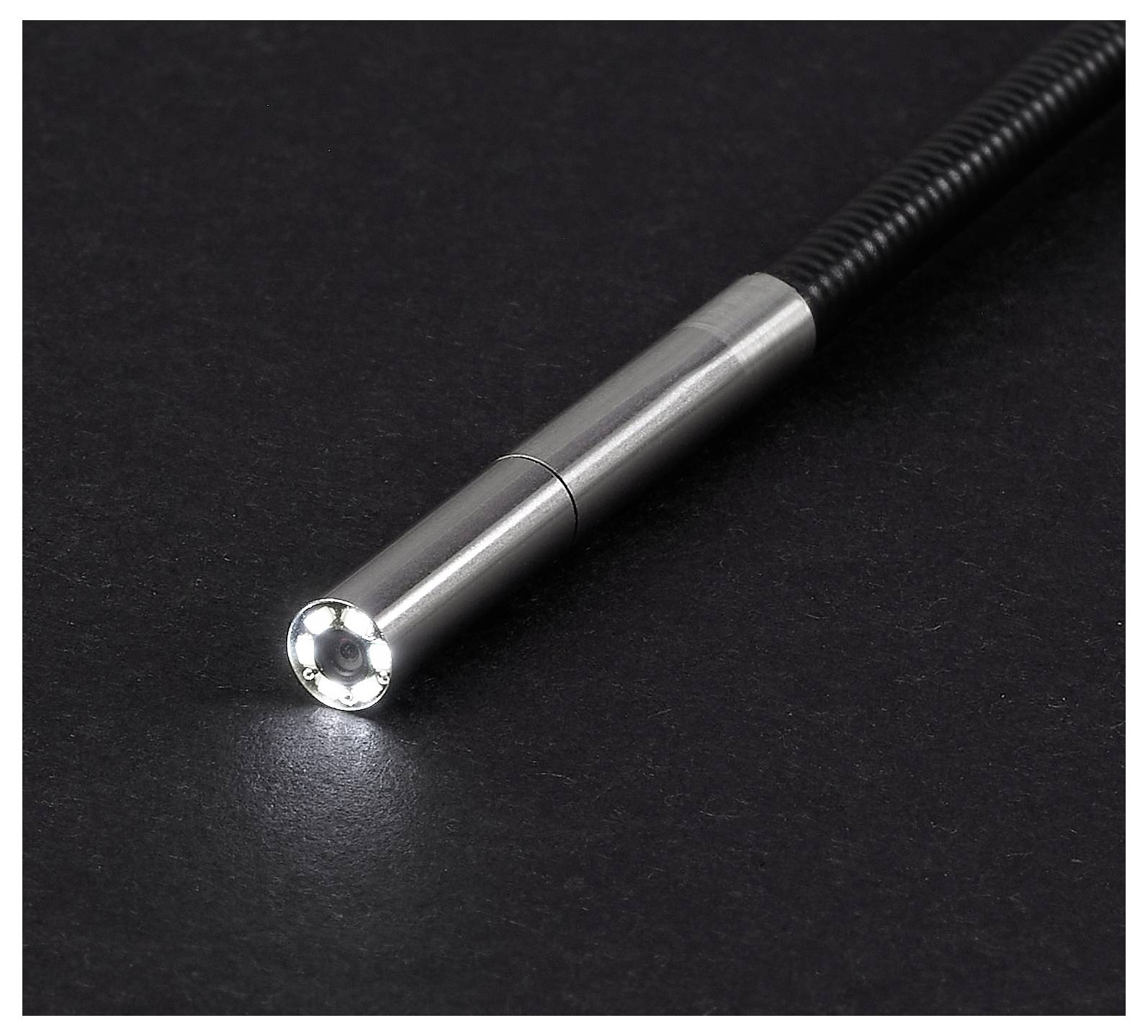 Nahaufnahme einer metallischen flexiblen Inspektionskamera-Sonde auf einer schwarzen Oberfläche, mit dem runden beleuchteten Objektiv nach vorne gerichtet.