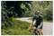 Eine Person fährt auf einem sich schlängelnden Weg durch einen üppig grünen Wald Fahrrad, trägt einen Helm, Sonnenbrille und Radkleidung und wirkt konzentriert.