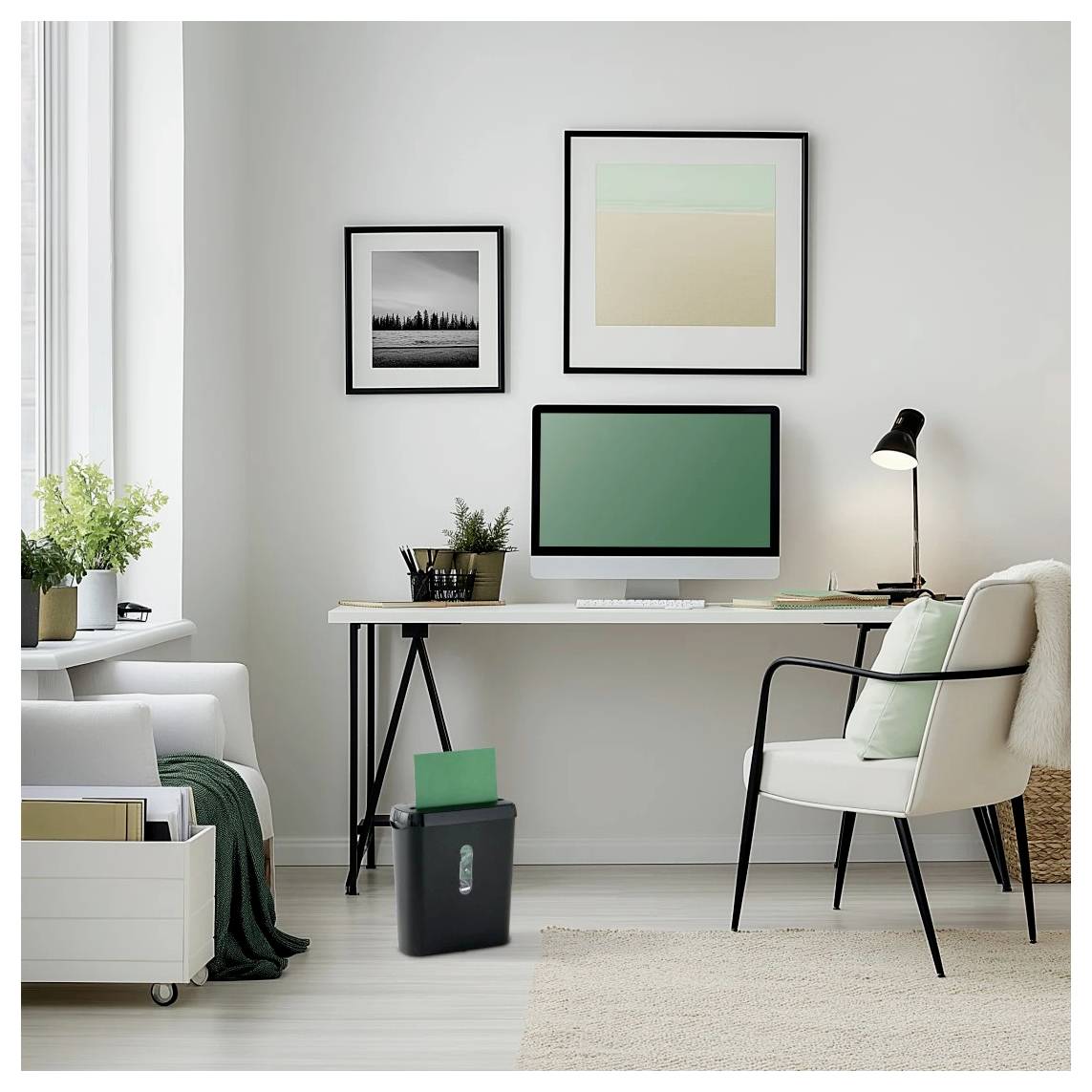 Home Office mit einem Schreibtisch, auf dem ein Computer steht, ein grüner Ordner im Aktenvernichter liegt und Wandkunst hängt. Ein gemütlicher Stuhl und eine Lampe vervollständigen die Einrichtung.