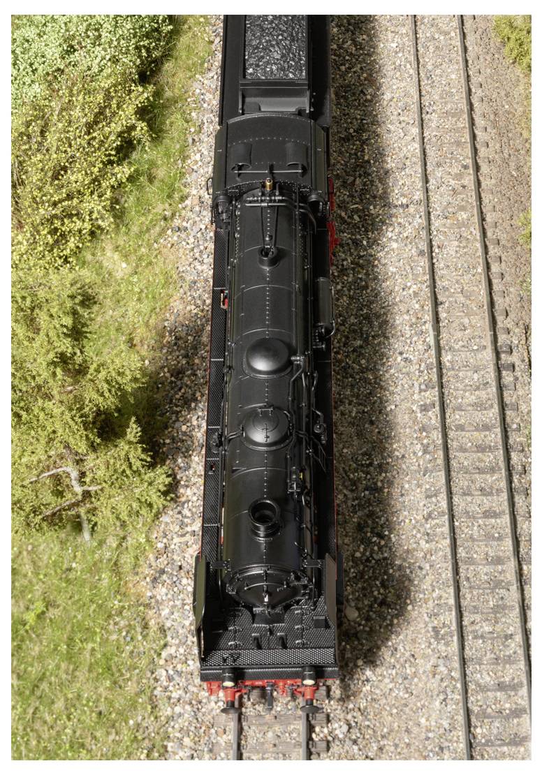 Luftaufnahme einer Modell-Dampflokomotive in Schwarz auf Schienen, umgeben von grünem Blattwerk, mit detailreicher Schienengestaltung.