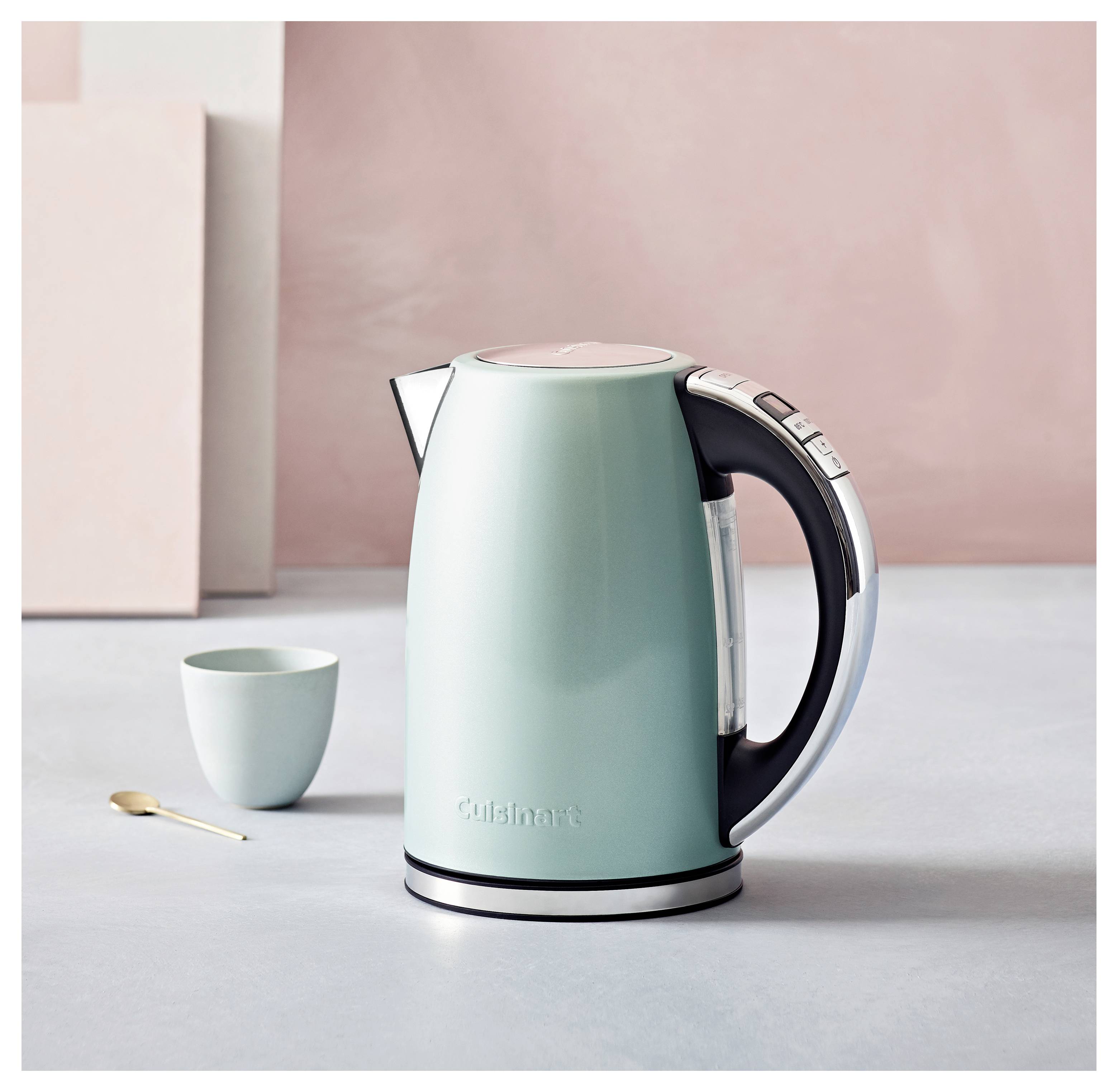 Eine minzgrüne elektrische Wasserkocher mit schwarzem Griff und digitaler Steuerung steht auf einer grauen Oberfläche neben einer kleinen passenden Tasse und einem Löffel.