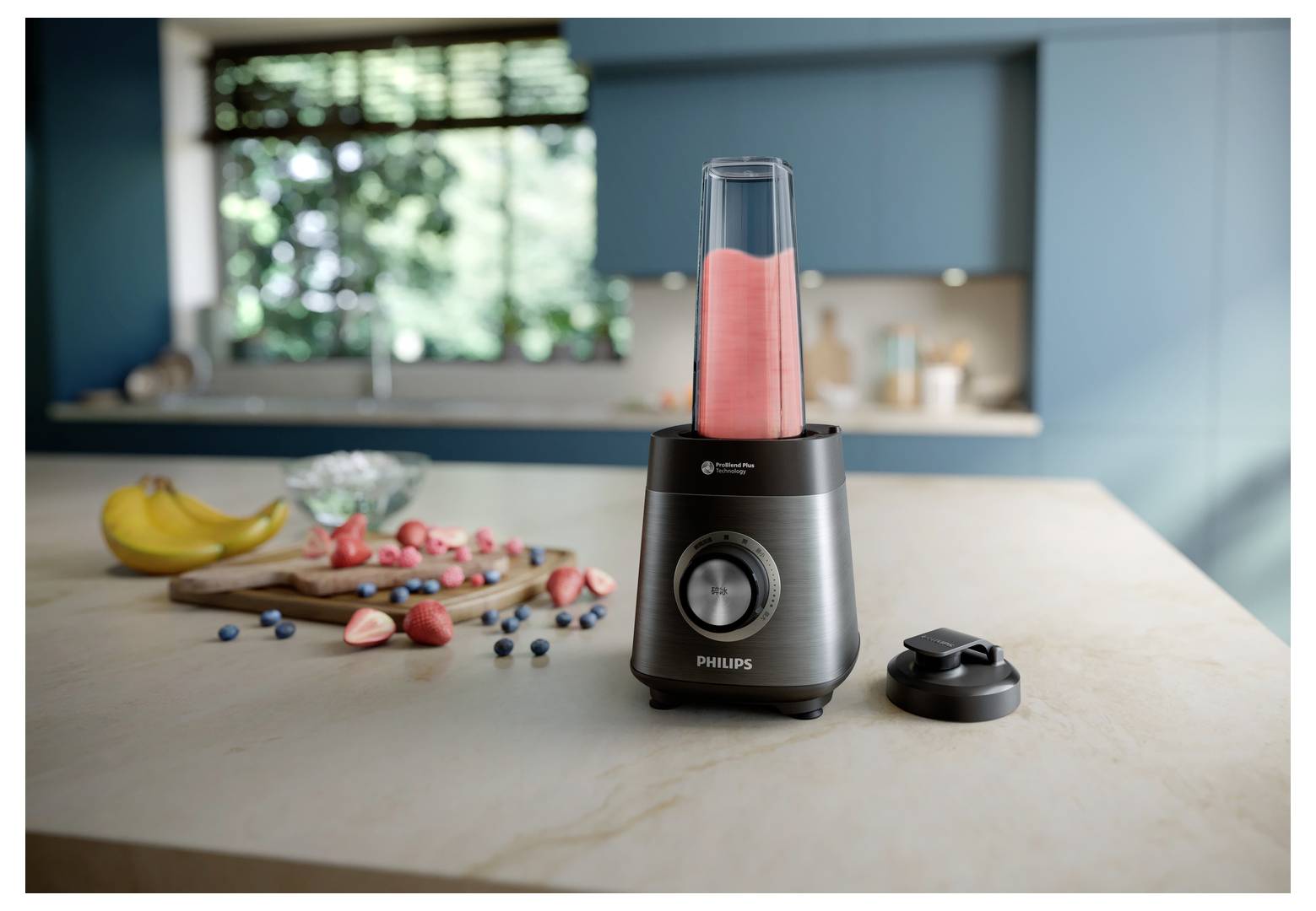 Ein Standmixer auf einer Küchenarbeitsplatte, gefüllt mit einem rosa Smoothie. In der Nähe liegen geschnittene Erdbeeren, Blaubeeren und Bananen. Moderne Kücheneinrichtung.