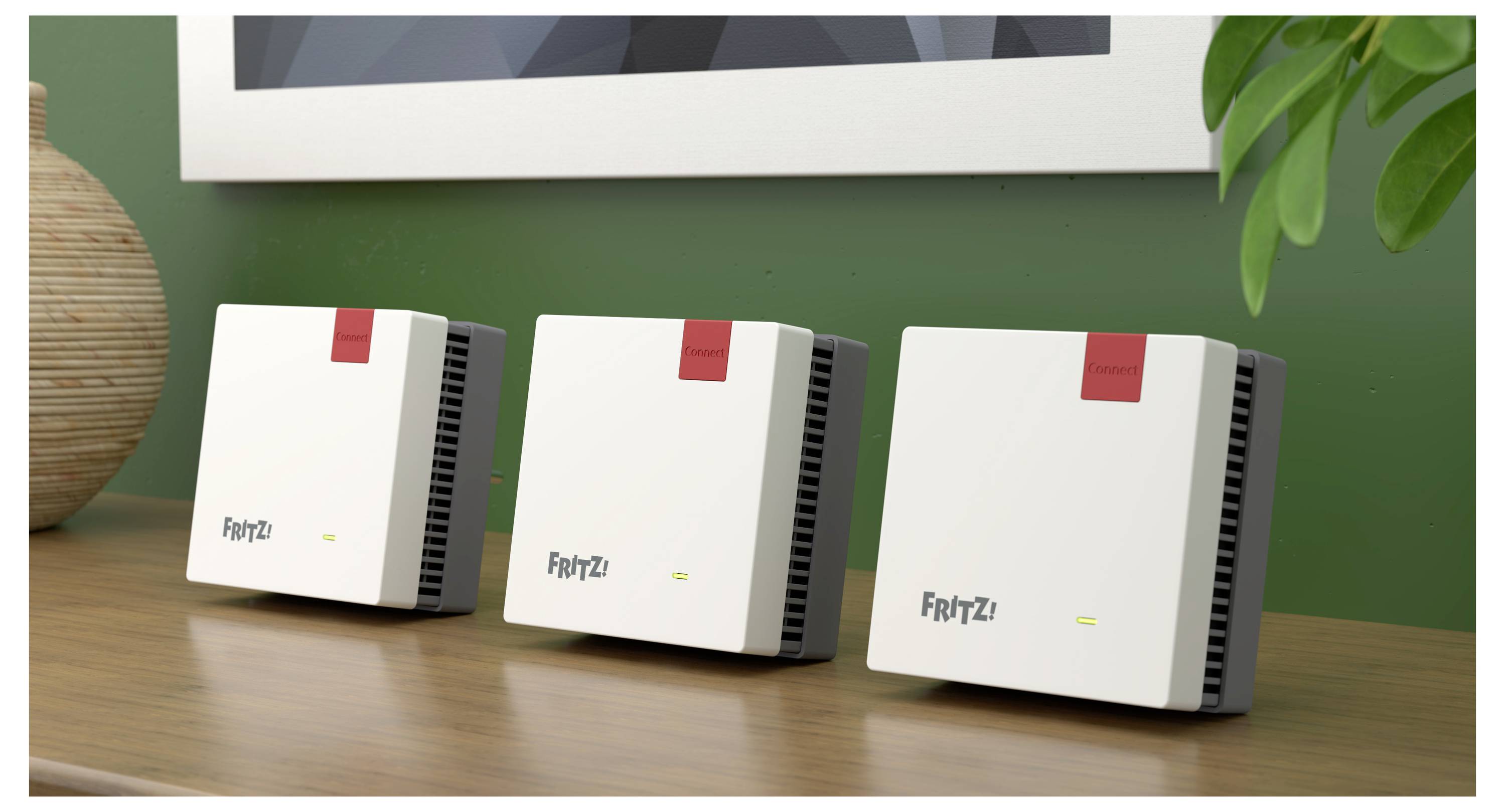Drei identische weiße Netzwerkgeräte, jeweils mit der Aufschrift "FRITZ!" und grünen sowie roten Anzeigen, liegen auf einer Holzoberfläche.