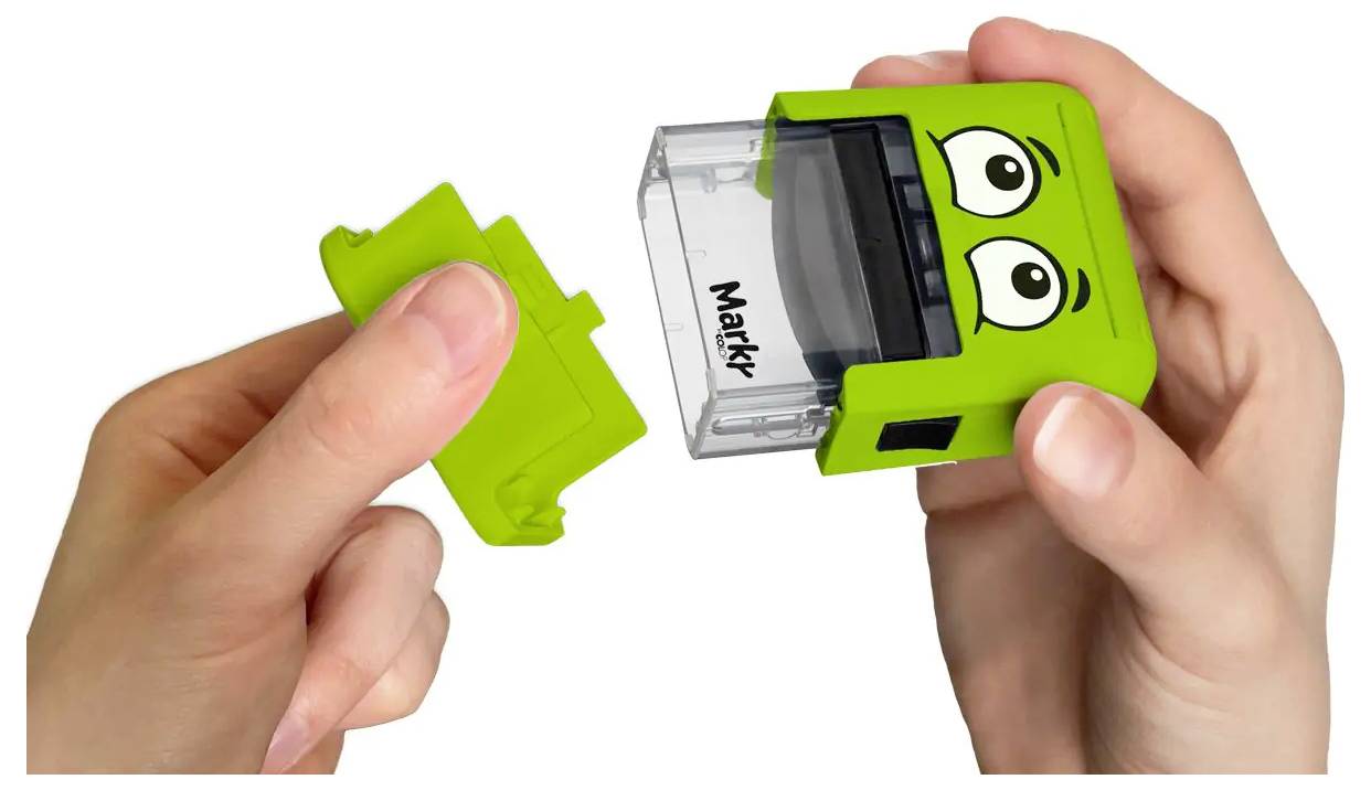 Zwei Hände, die einen grünen Selbstfärber-Stempel mit Cartoon-Augen zusammenbauen. Eine Hand hält eine Plastikkomponente, während die andere die Stempelbasis hält.
