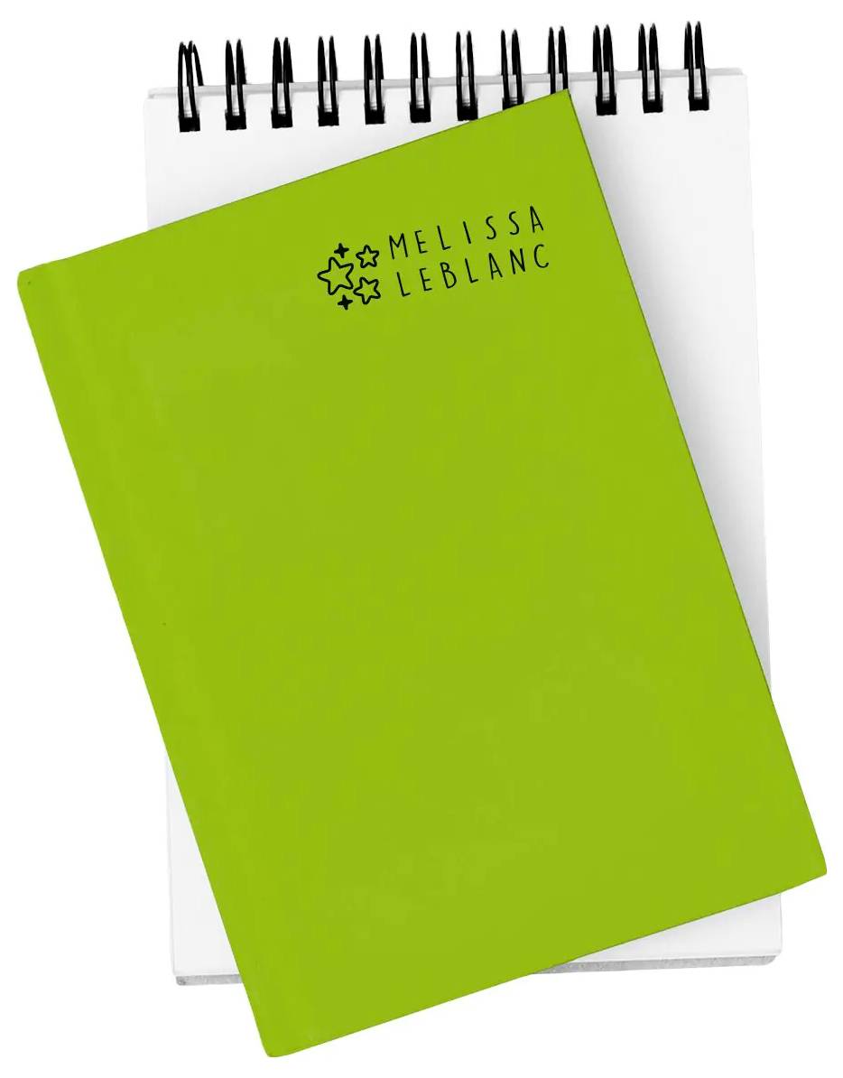 Ein grünes Notizbuch mit dem Aufdruck 'Melissa LeBlanc' auf dem Einband liegt auf einem spiralgebundenen Notizblock, die beide leer sind.