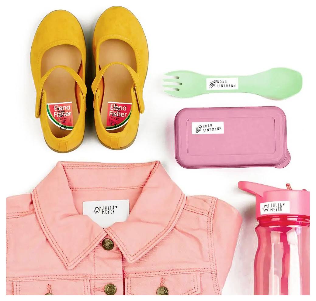Kinderutensilien umfassen gelbe Schuhe, pinke Brotdose, grünen Esslöffel, beschriftete Jacke und pinke Wasserflasche, wobei personalisierte Etiketten hervorgehoben werden.