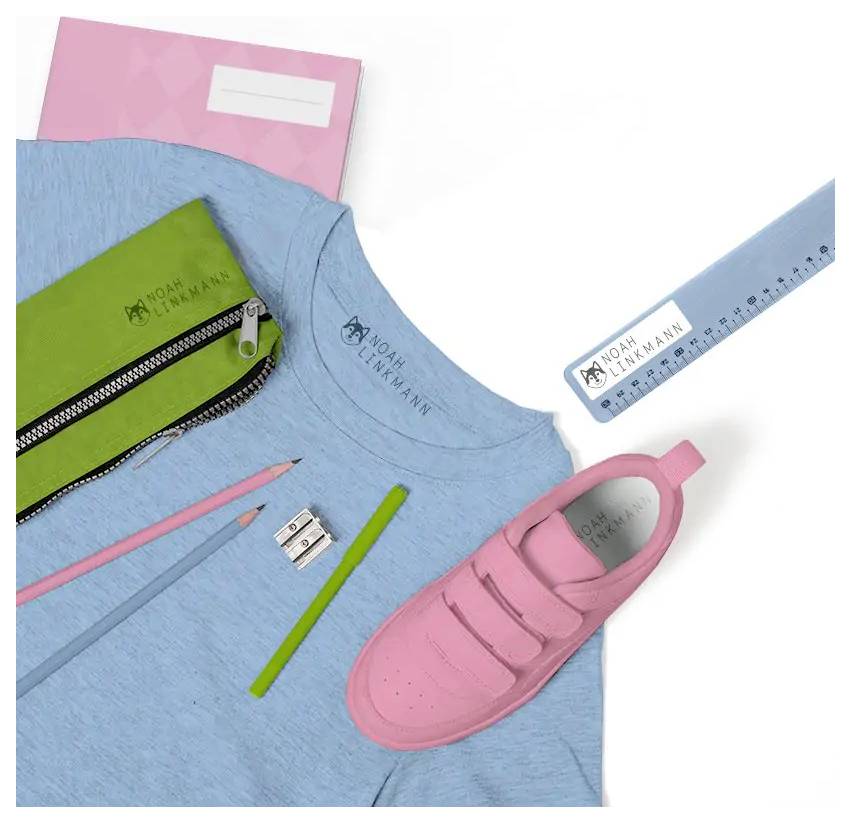 Blaues Hemd mit Markenlogo, rosa Kleinkinderschuh, grüne Federmappe, rosa Notizbuch, blaues Lineal, Bleistifte und Anspitzer künstlerisch angeordnet.