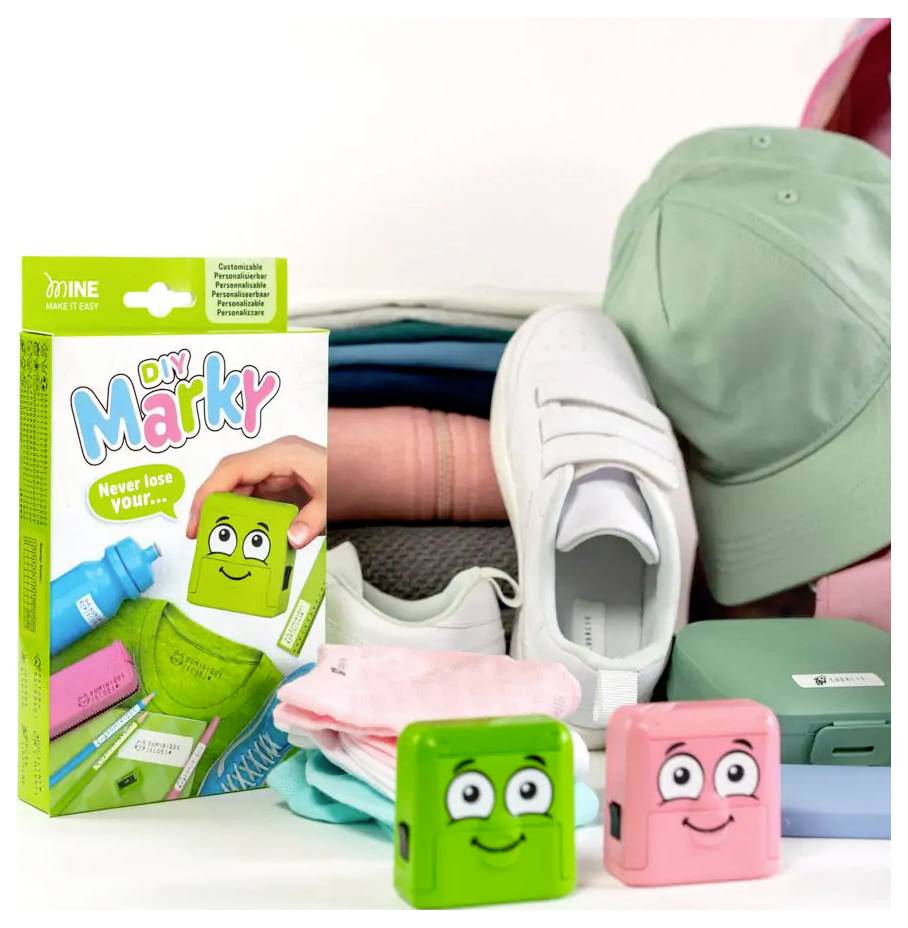 DIY Marky Stempel-Sets mit grünen und pinken Stempeln mit lächelnden Gesichtern; platziert neben gefalteten Kleidungsstücken, einer grünen Kappe und weißen Schuhen.