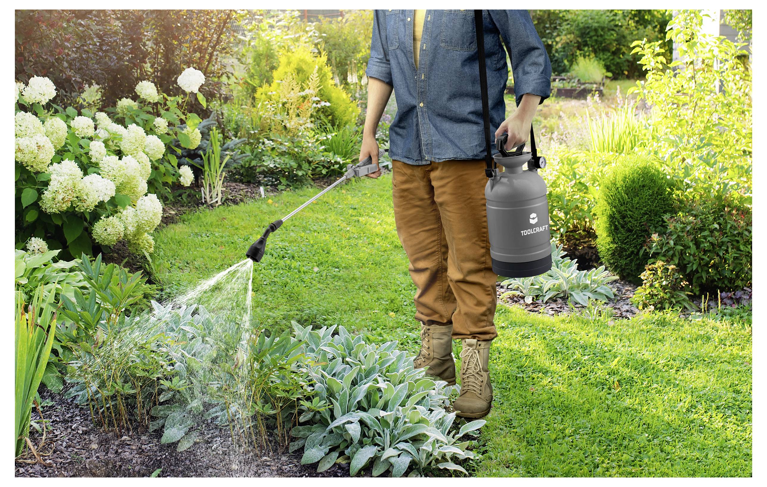 Eine Person benutzt eine Gartenspritze, um Pflanzen in einem üppigen Garten mit verschiedenen Blumen und Grünflächen zu bewässern.