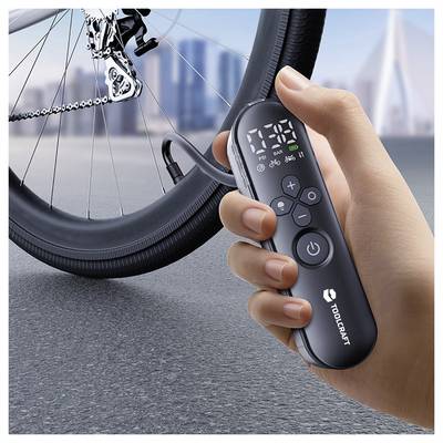 Hand, die eine TOOPCRAFT Elektrofahradpumpe mit digitaler Druckanzeige neben einem Fahrradreifen und Ventil hält.