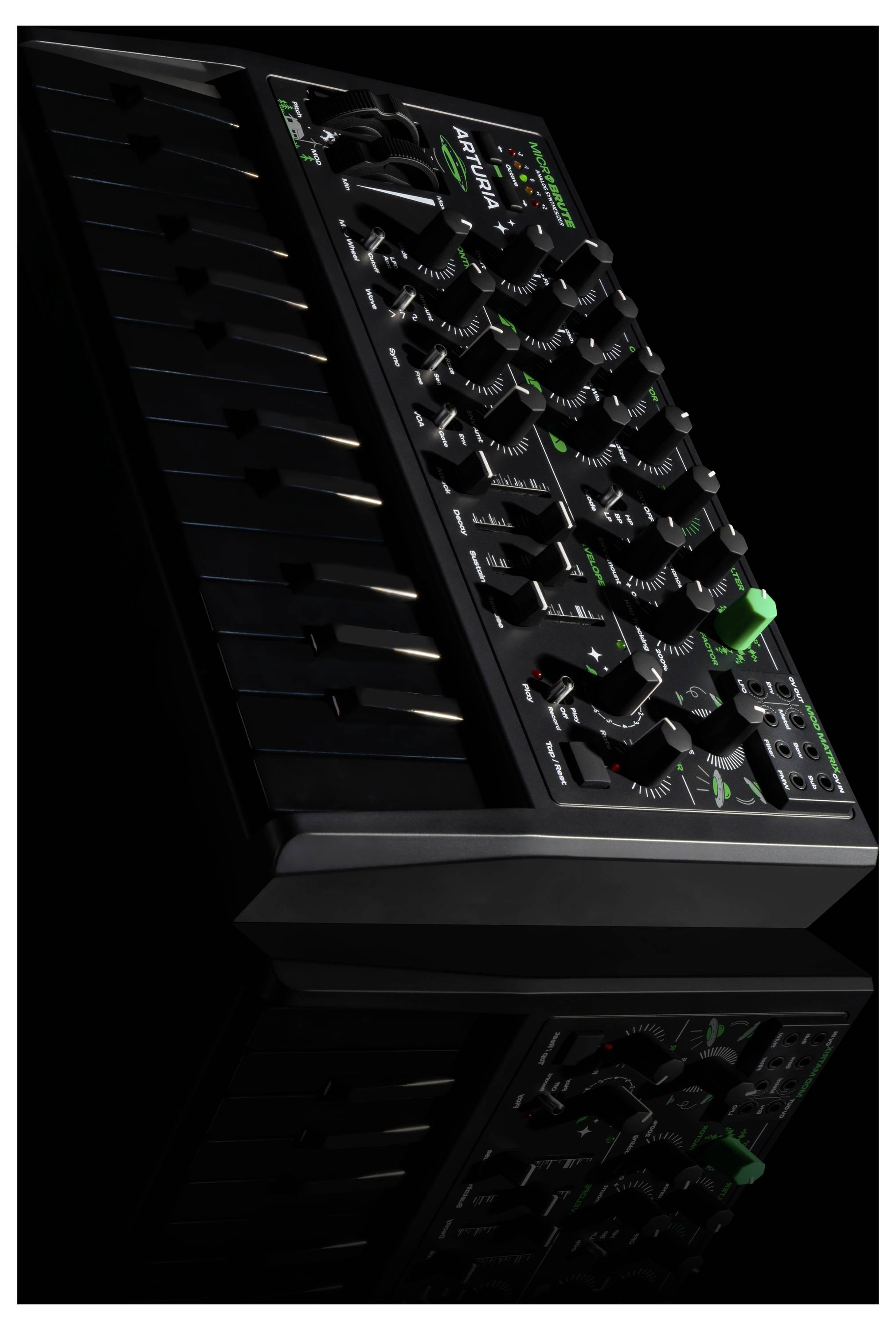 Ein kompakter schwarzer Synthesizer mit zahlreichen Reglern und Tasten, aus einem schrägen Blickwinkel, der auf einer reflektierenden schwarzen Oberfläche steht.