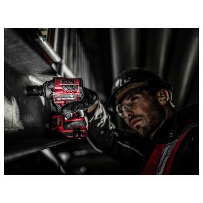 Ein Mann mit Sicherheitsausrüstung verwendet eine rote Bohrmaschine an einem Metallträger und betont damit Bau- oder industrielle Arbeit.