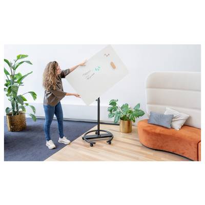 Eine Person richtet eine rotierende Whiteboardtafel mit der Aufschrift "Projektplanung" in der Nähe eines modernen Sofas und Pflanzen in einem zeitgemäßen Büro ein.