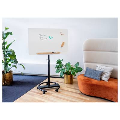 Eine Whiteboard auf einem Ständer zeigt den Text "Apotheken" und "Erfahrung" mit einem blauen Kreislogo. In der Nähe befinden sich Topfpflanzen und ein orangefarbenes Sofa.