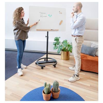 Eine Frau zeigt auf ein Whiteboard mit den Worten "Marketingplan-Ziele", während ein Mann aufmerksam zuhört. Indoor-Büroumgebung.
