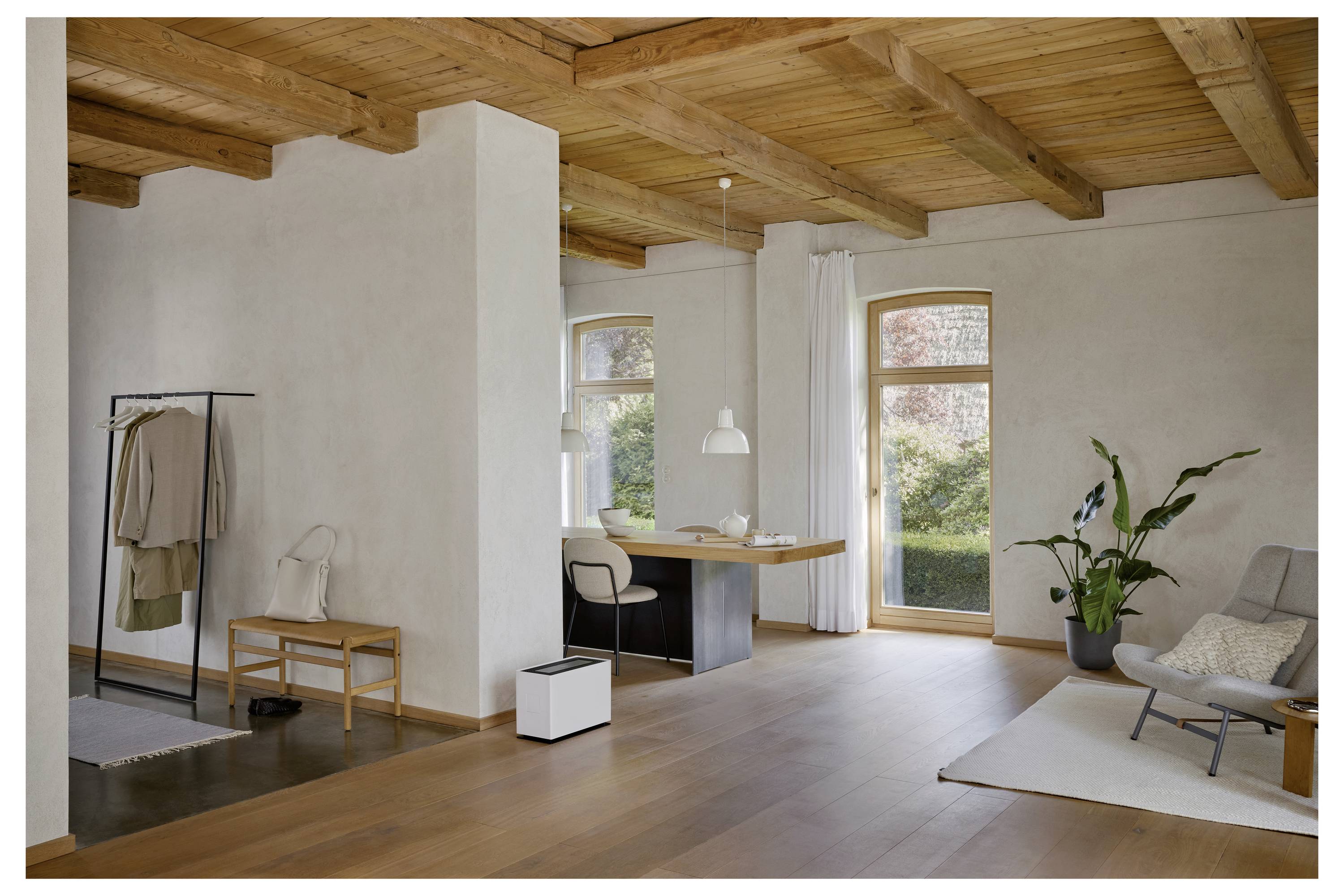 Ein moderner, minimalistischer Wohnbereich mit Holzdeckenbalken, einem großen Fenster, einer Pflanze, einem Schreibtisch mit Lampe und einer Sitzgelegenheit.