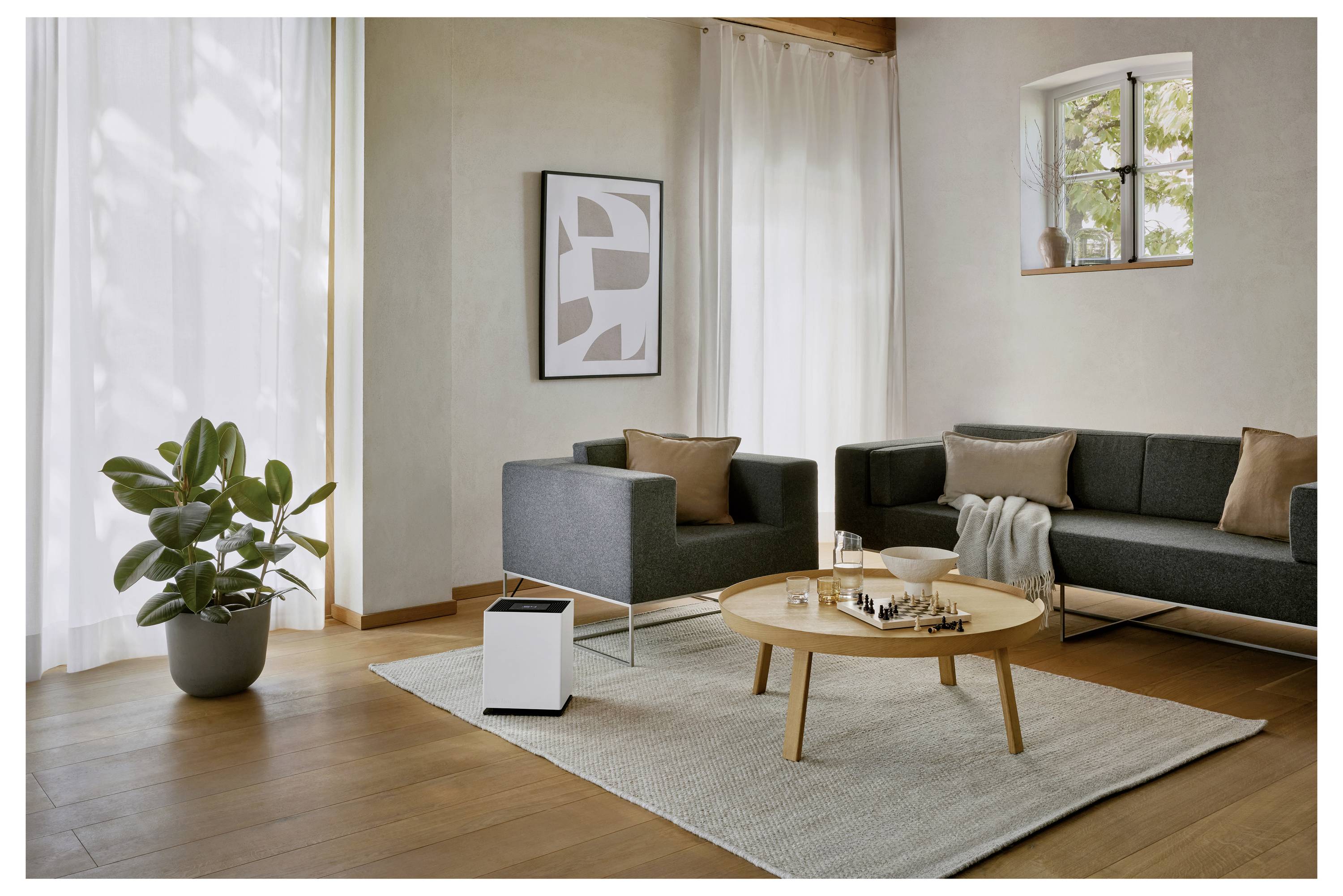 Ein modernes Wohnzimmer mit grauen Sofas, einem Holzkaffeetisch, einer Topfpflanze und einem abstrakten gerahmten Kunstwerk. Licht strömt durch ein Fenster herein.