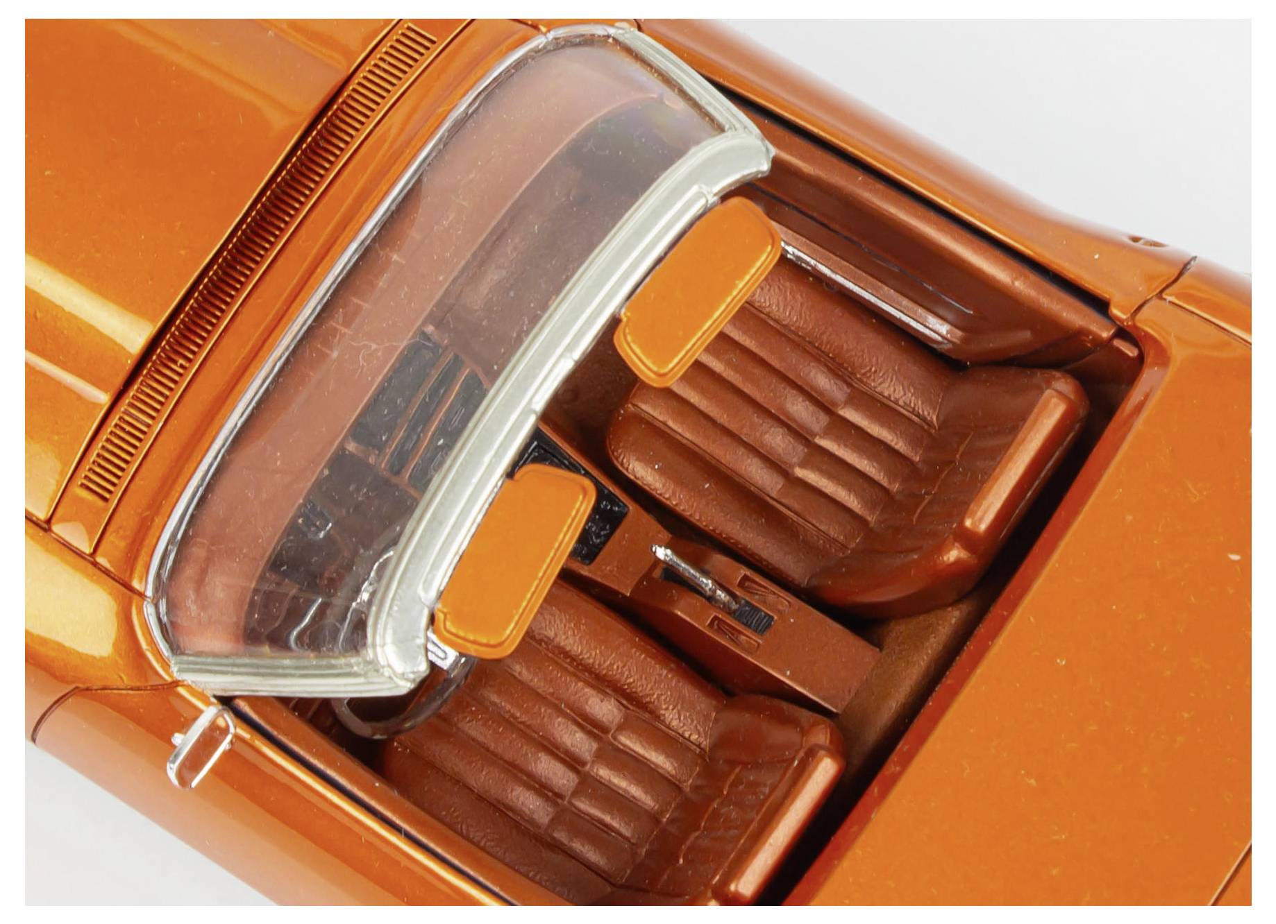 Draufsicht eines Miniatur-Orange-Cabrios, das zwei braune Sitze und detaillierte Innenausstattungsmerkmale präsentiert.