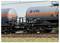 Zwei graue Kesselwagen mit orangefarbenen Streifen und dem Logo von 'VTG', die auf Eisenbahnschienen in einer Außenumgebung positioniert sind.