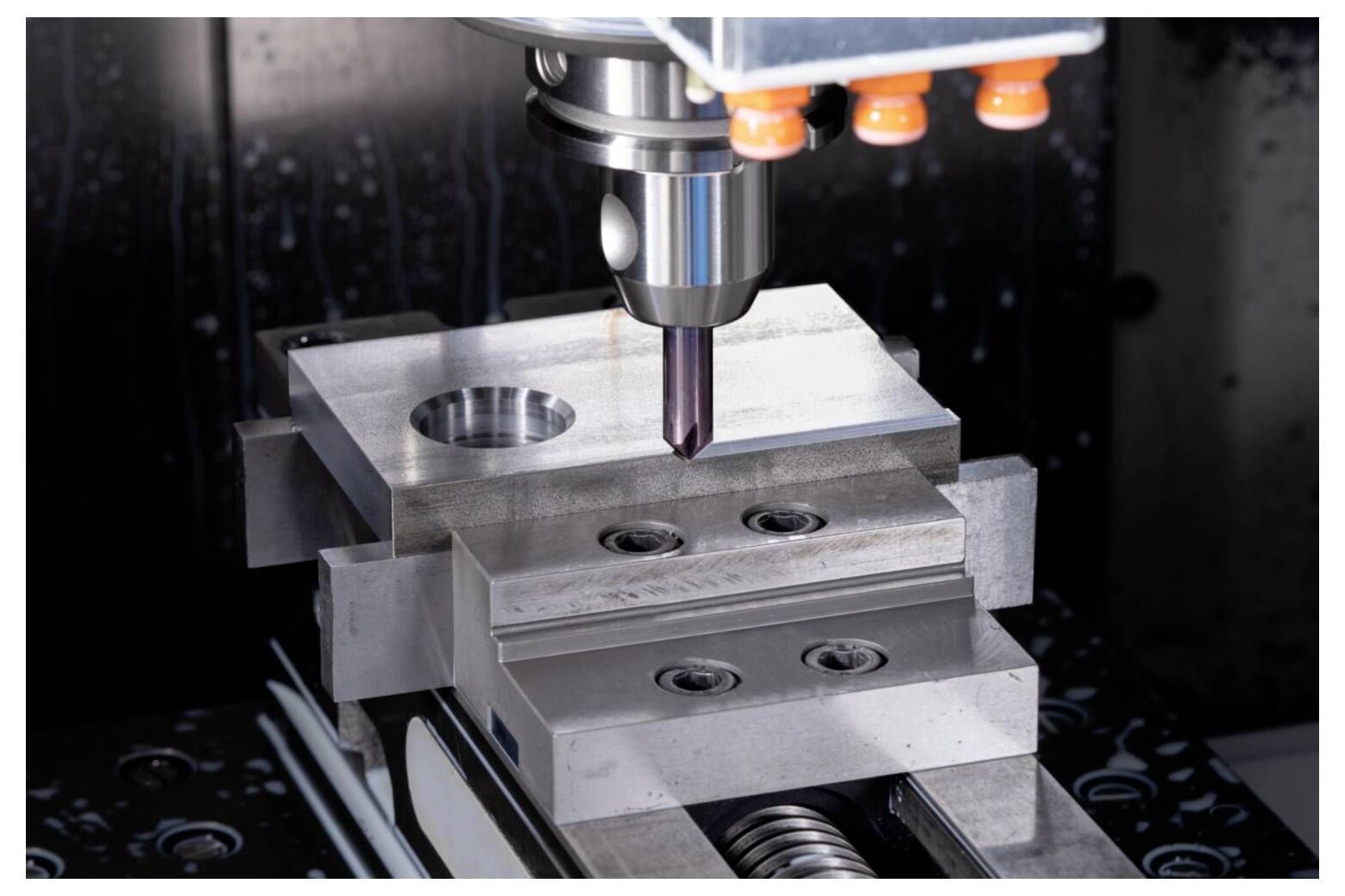 Eine CNC-Maschine bohrt ein Metallstück mit Präzision. Die Aufnahme zeigt den Maschinenkopf, die Metallplatte, die Klemmen und das Bohrloch in Nahaufnahme.