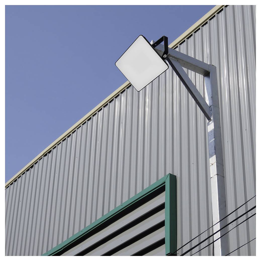 Ein großes industrielles Metallgebäude mit einer quadratischen, an der Wand montierten Leuchte vor einem klaren blauen Himmel.
