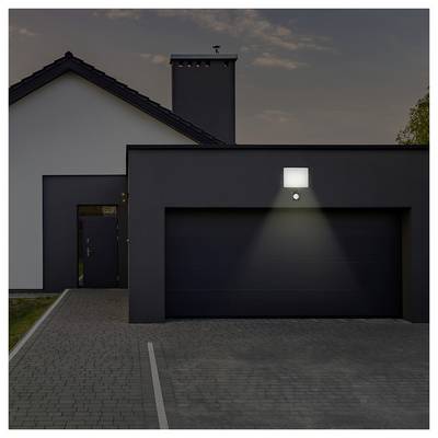 Eine moderne Hausaußenansicht mit einer einzelnen Lampe über der Garagentür, die die Einfahrt in der Abenddämmerung beleuchtet.