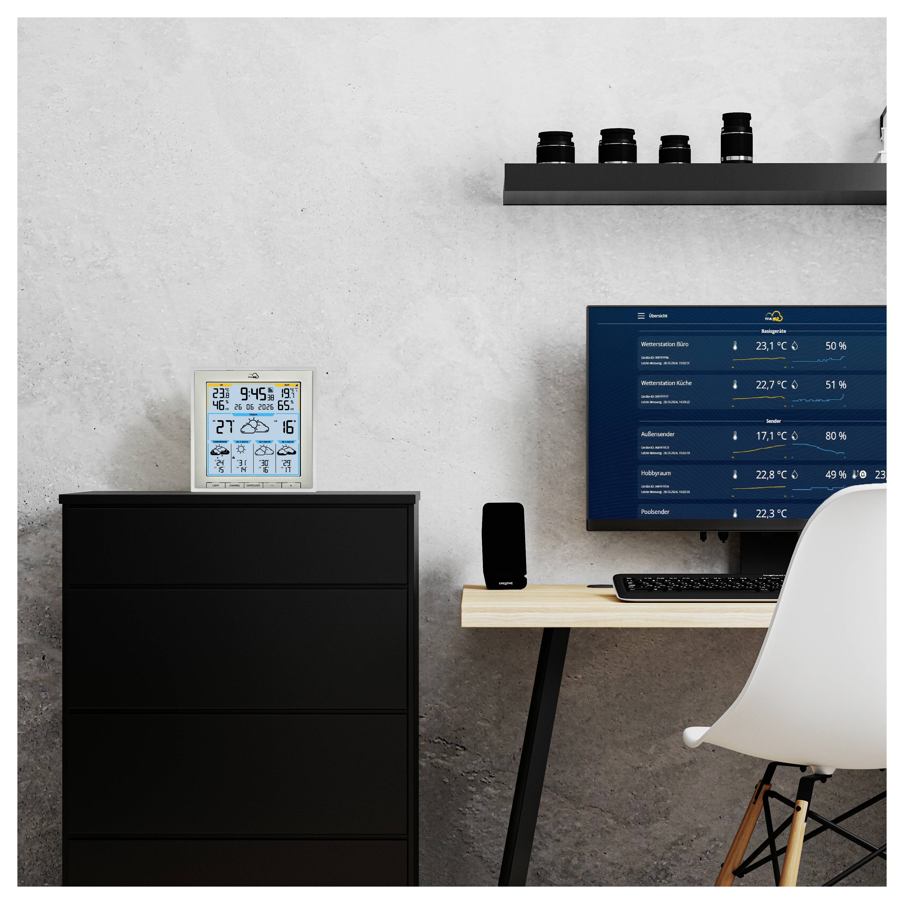 Arbeitsplatz mit schwarzem Stuhl, minimalistischer Dekoration, elektronischer Wetteranzeige mit Temperatur- und Luftfeuchtigkeitsanzeige, schwarze Regale mit Kameraobjektiven.