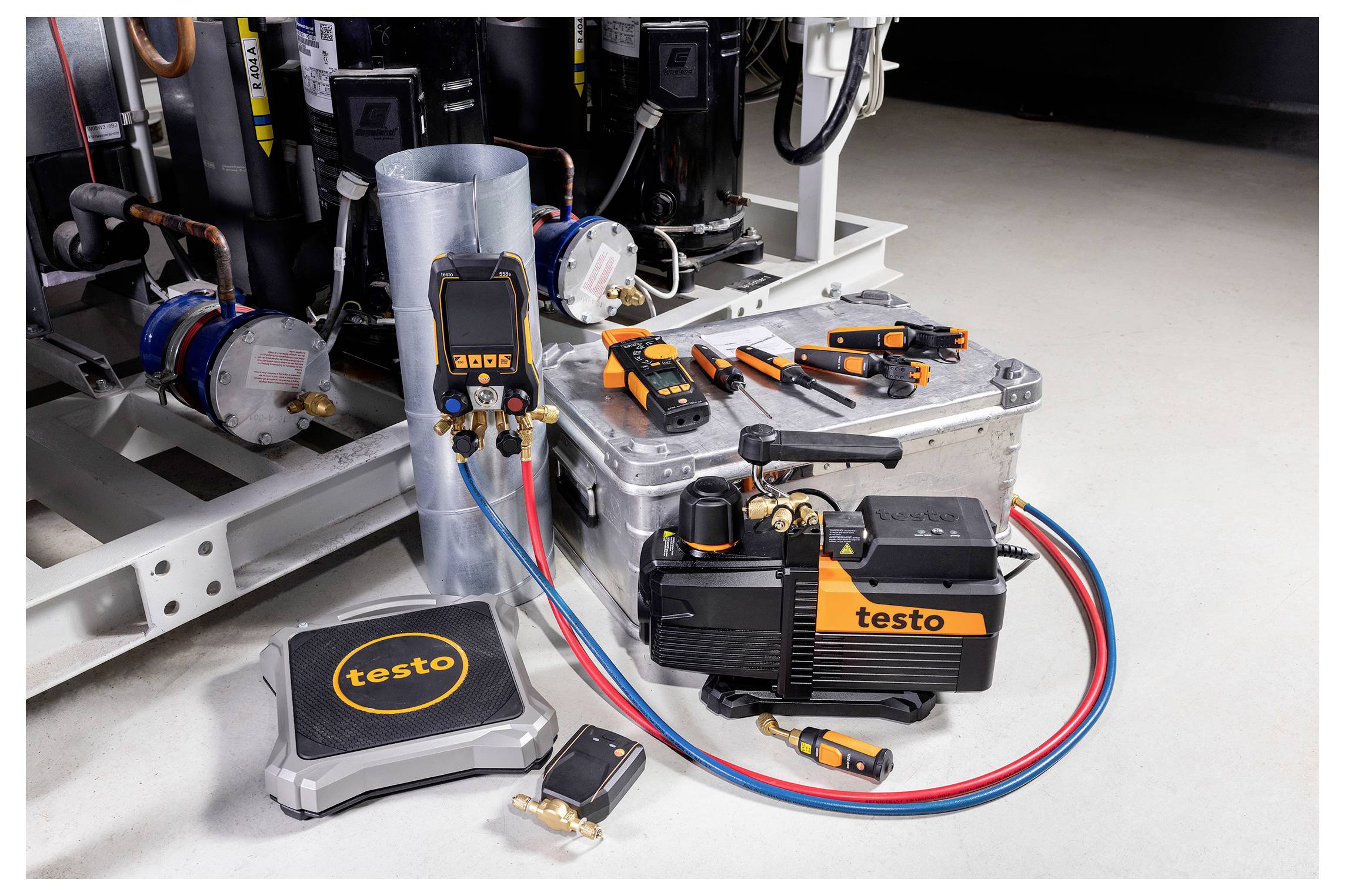 Testo HVAC-Werkzeugsatz auf dem Boden, einschließlich Vakuumpumpe, digitalem Verteiler und verschiedenen Sensoren, neben HVAC-Ausrüstung und einem Metalllüftungskanal.