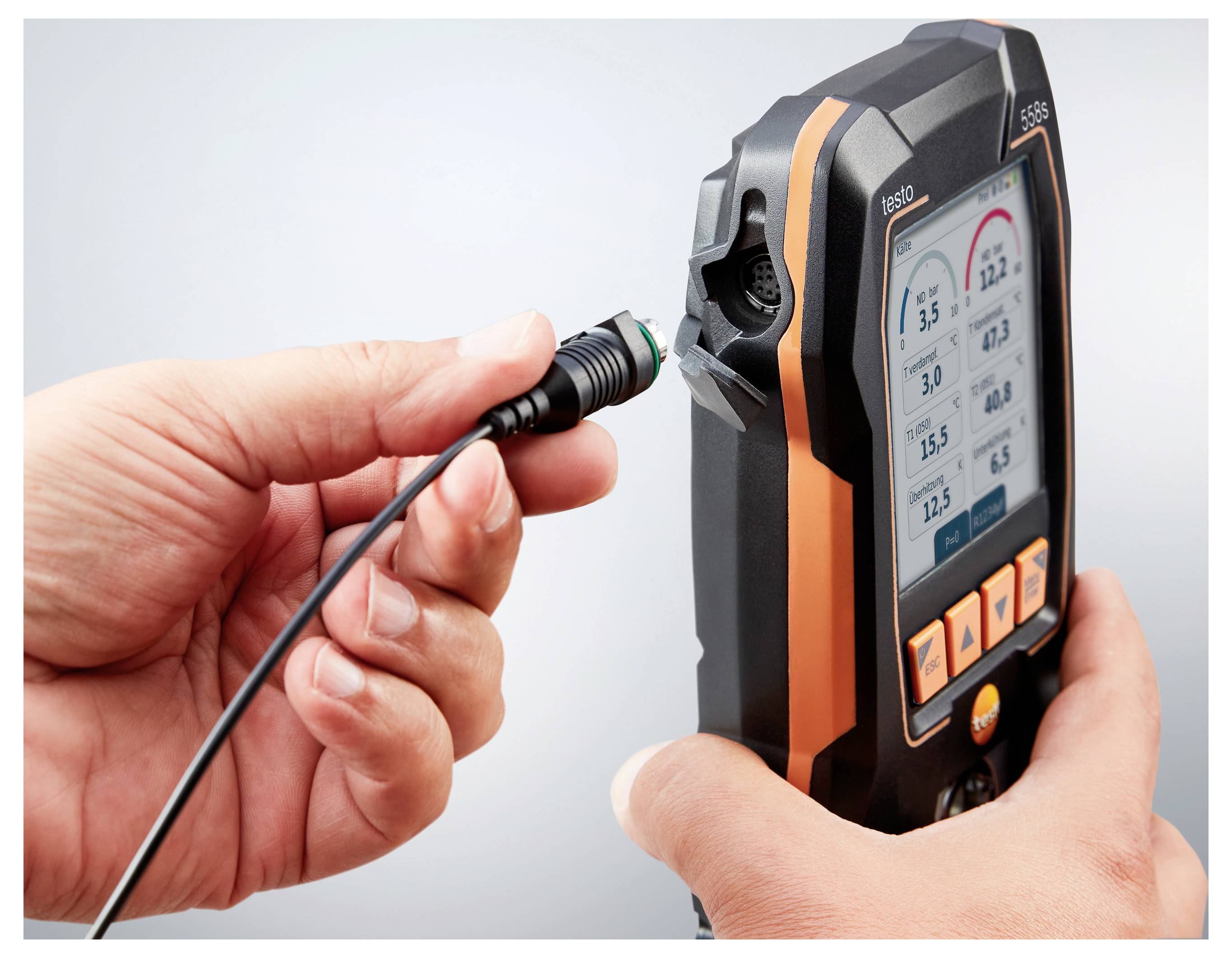 Eine Hand, die einen elektrischen Stecker hält, steht kurz davor, ihn mit einem tragbaren Gerät zu verbinden, das Messungen auf seinem Bildschirm anzeigt.