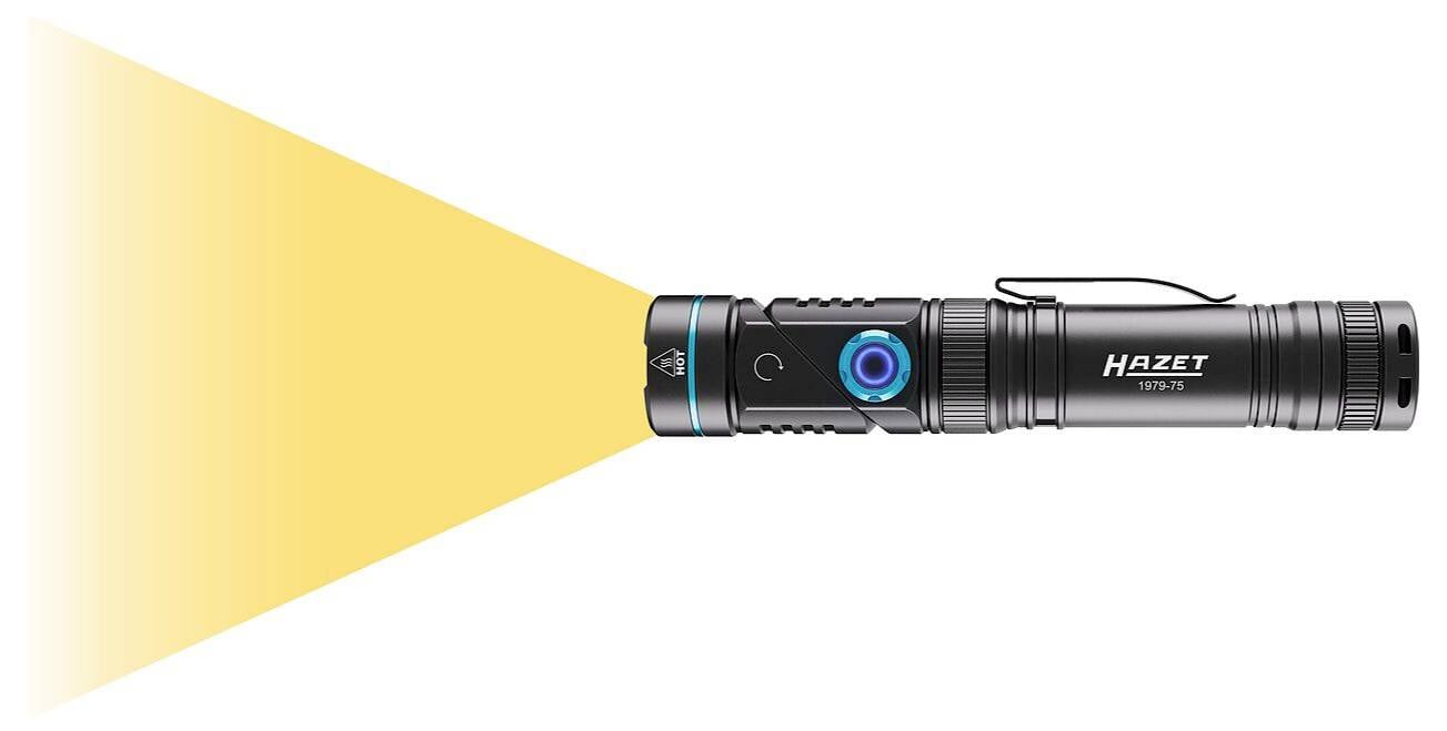 Eine tragbare schwarze Taschenlampe, die einen hellen gelben Lichtstrahl nach links projiziert, mit einem blauen Knopf und dem 'Hazet' Logo an ihrer Seite.