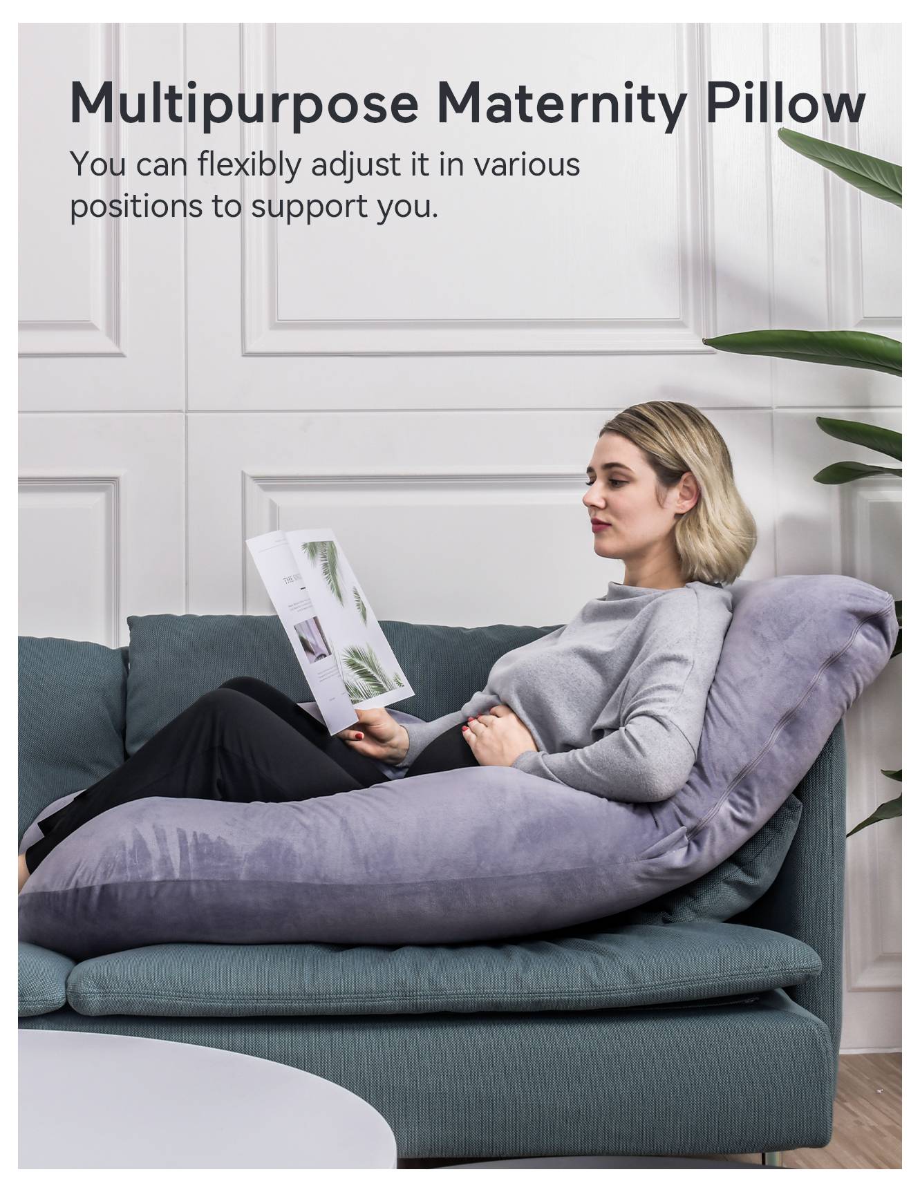 Frau entspannt auf einem Sofa, die sich an ein großes, graues Schwangerschaftskissen lehnt und ein Buch liest. Text: Multifunktionales Schwangerschaftskissen.