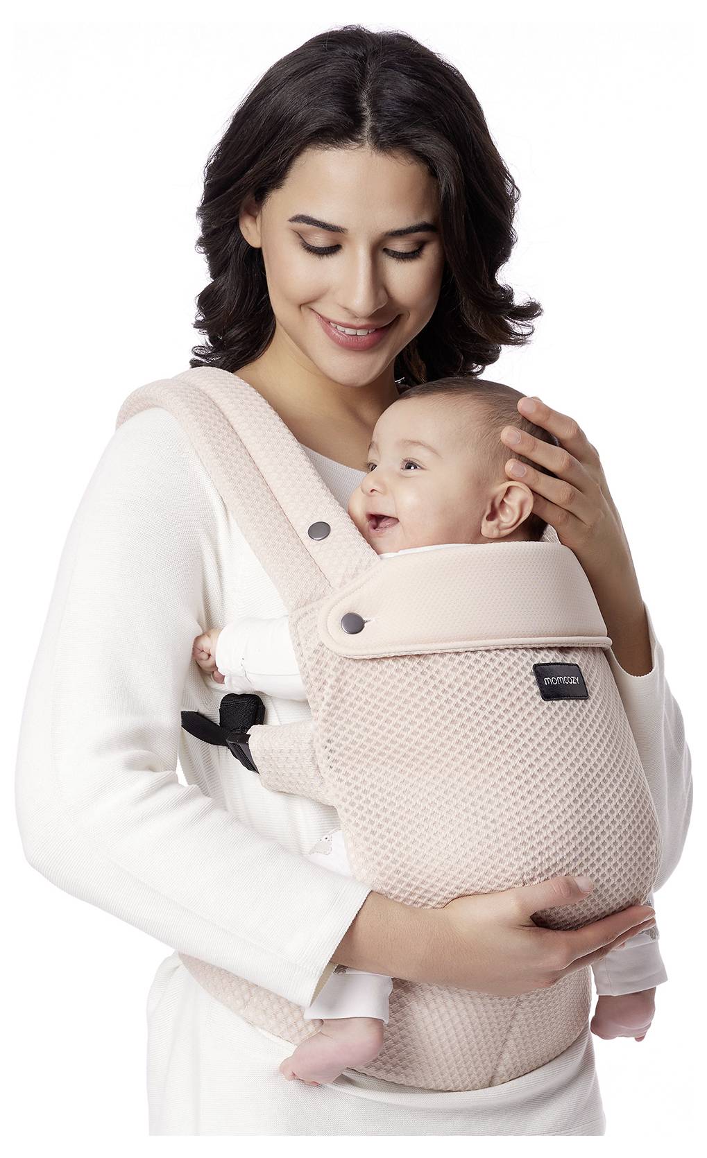 Eine Frau lächelt und hält ein Baby in einem hellrosa Tragegurt. Das Baby blickt nach oben und lächelt ebenfalls. Die Umgebung ist neutral.