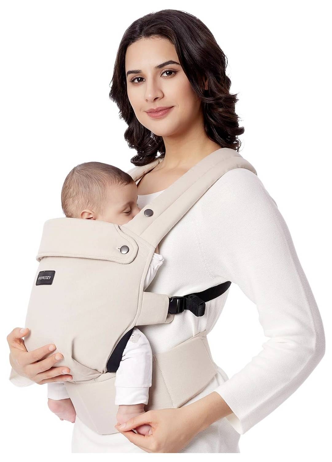 Eine Frau in einem weißen Hemd hält ein schlafendes Baby in einem beigen Babytrage und wirkt zufrieden.