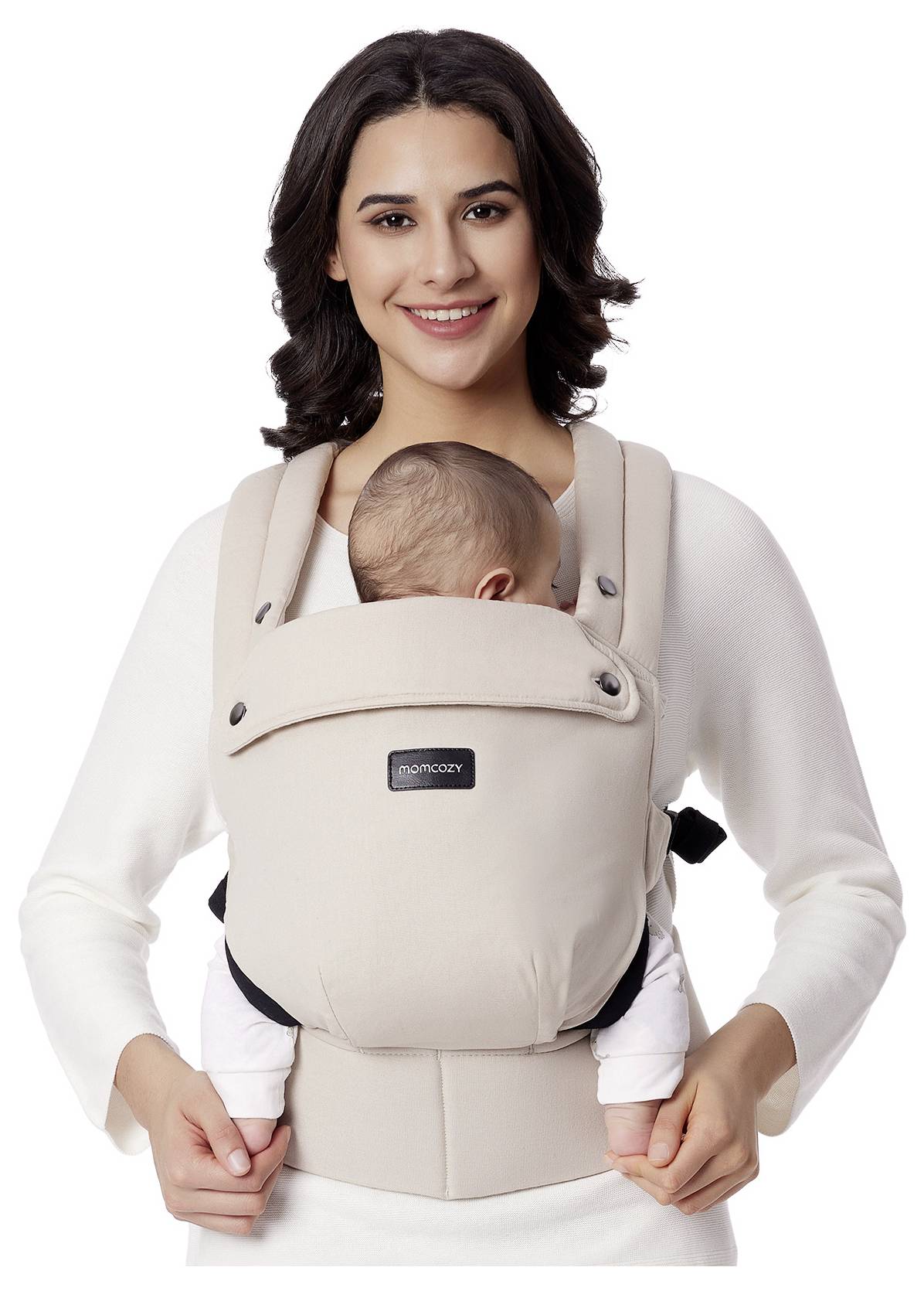 Eine Person lächelt, während sie ein Baby mit Blick nach innen in einem beigen Babytrage trägt.