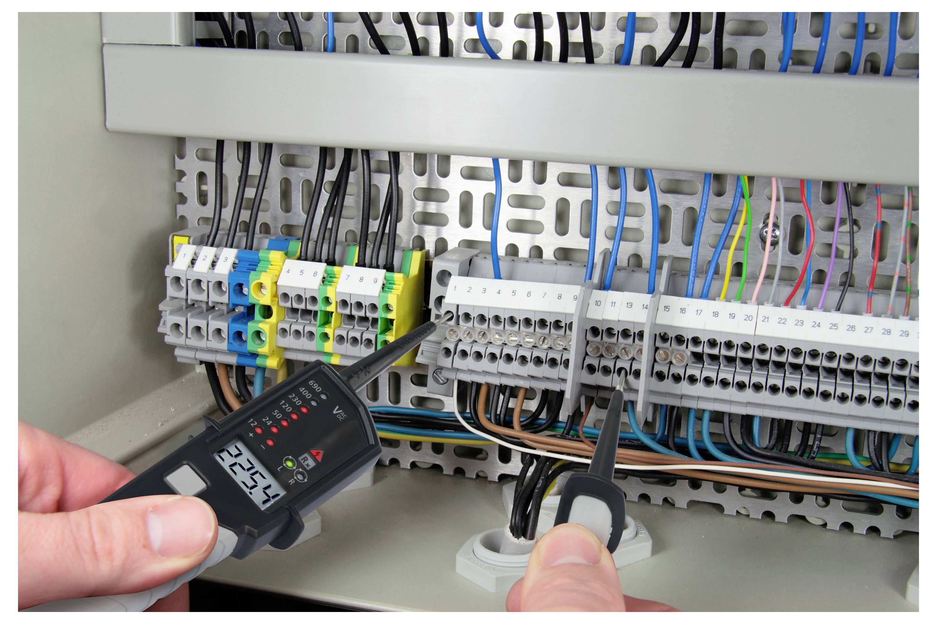Techniker testet ein elektrisches Steuergerät mit einem digitalen Messinstrument, während er die Messleitungen in der Nähe von Verdrahtung und Klemmleisten hält.