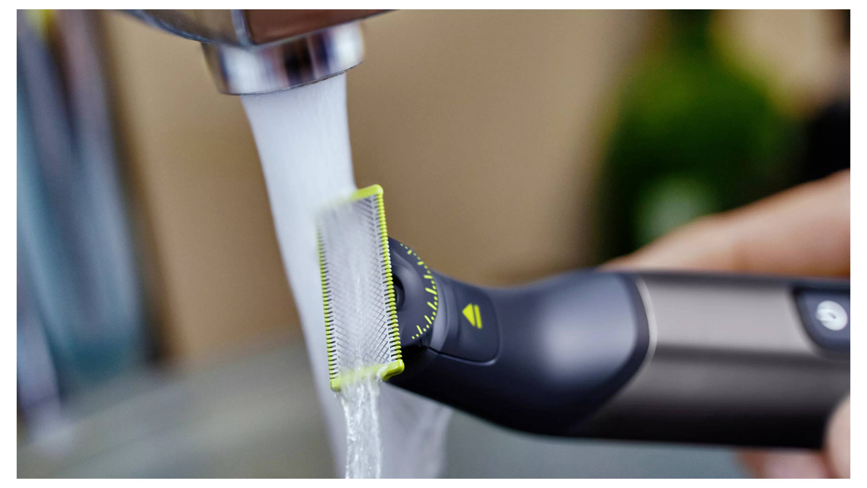 Eine Hand spült einen Trimmerkopf unter einem laufenden Wasserhahn, was eine einfache Reinigung des Pflegergeräts andeutet.
