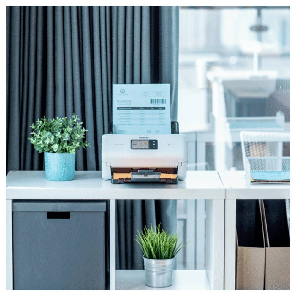 Ein Drucker auf einem weißen Regal mit einem Dokument, das mit "Rechnung" beschriftet ist, neben einer Topfpflanze und einer Aufbewahrungsbox in einer modernen Büroumgebung.