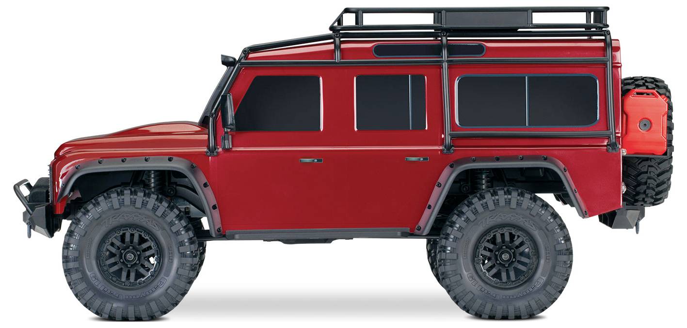 Ein roter Geländewagen mit großen, robusten Reifen und Dachträgern ist von der Seite zu sehen. Das Fahrzeug hat einen Benzinkanister am Heck angebracht.