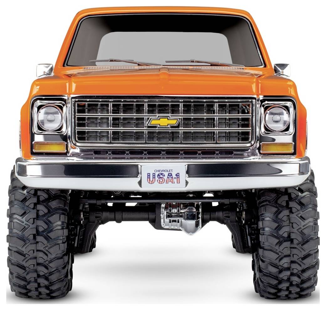 Orangefarbener Chevrolet Pickup-Truck mit großen Geländereifen, Chromstoßstange und einem Nummernschild mit der Aufschrift 'USA1'. Frontansicht mit Kühlergrill und Emblem.