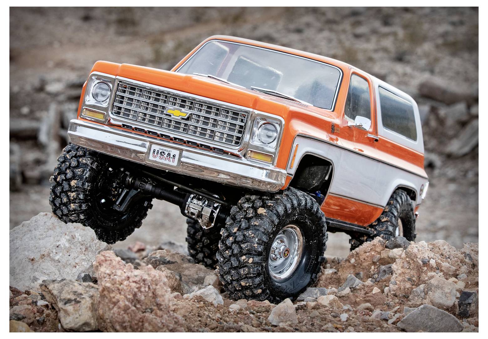 Ein robuster RC-Truck mit großen Geländereifen navigiert durch felsiges Terrain und präsentiert ein orangefarbenes und weißes Vintage-Design.