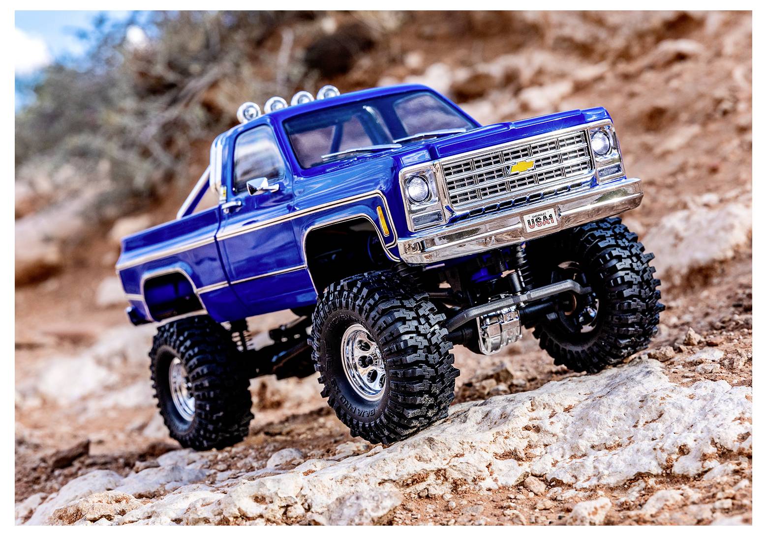 Ein detailliertes Modell eines blauen Pickup-Trucks mit überdimensionalen Reifen auf einem rauen, felsigen Gelände.