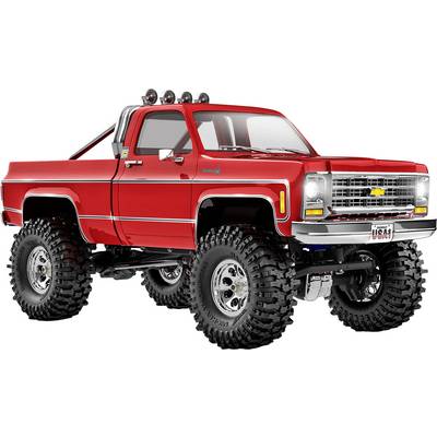 Ein knallroter restaurierter Vintage-Pickup-Truck mit großen Geländereifen, Chromdetails und einer Überrollbügel, vor einem einfarbigen weißen Hintergrund.