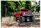 Ein roter Spielzeug-Monstertruck fährt über Erde und Blätter in einer Waldlandschaft und wirbelt mit seinen großen Reifen Staub auf.